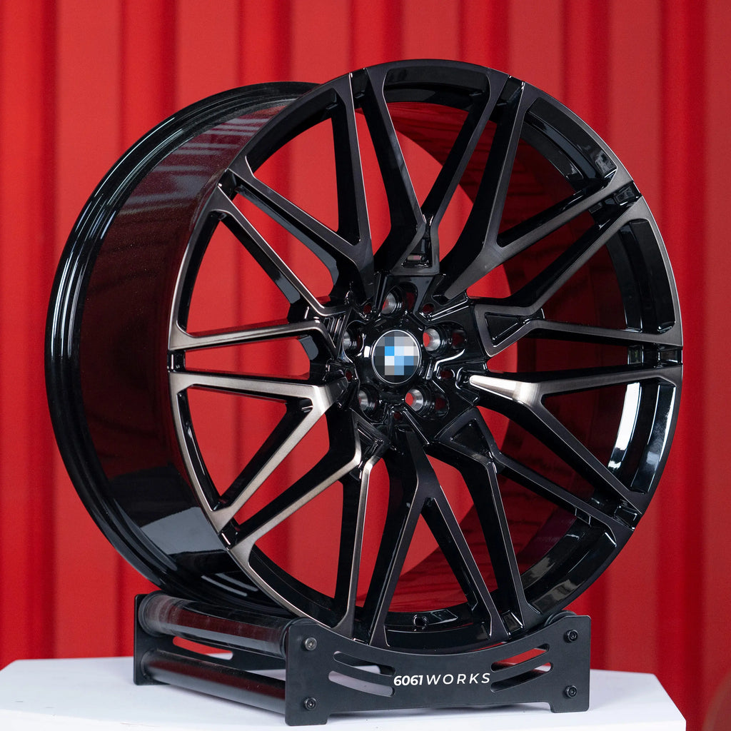 BMW X6 G06 22 inch custom forged wheels | OEM BMW 818M style Gloss Black with Machined Face Dark Coating, three-quarter view on display stand against red backdrop highlighting M-performance split-spoke geometry