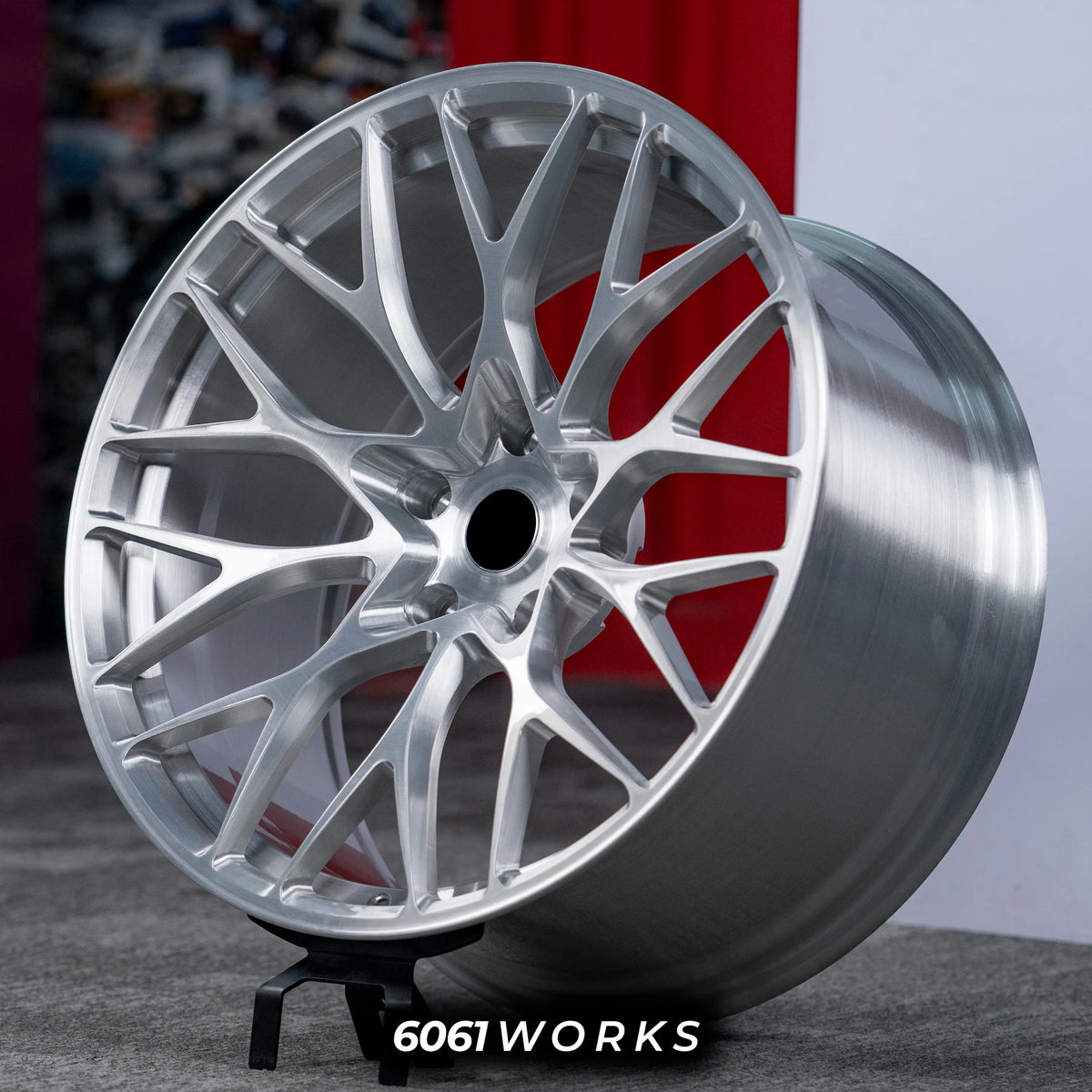 Porsche 911 992.2 Carrera 20 21 inch custom forged wheels | 520M style Brushed Silver finish, three-quarter view on display stand against red backdrop highlighting deep concave mesh-spoke geometry